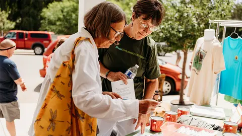 Two women look at papers at an outdoor table.