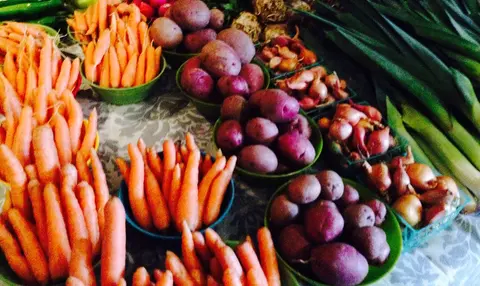 A display of fresh vegetables at a market, including carrots, potatoes, and greens.