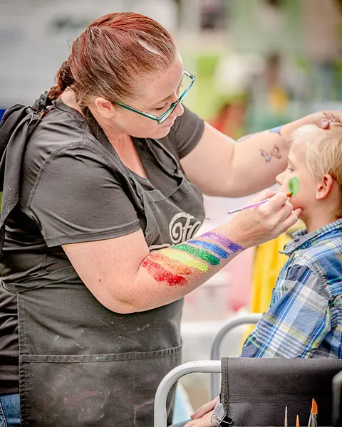 A woman paints a design on a child's face.