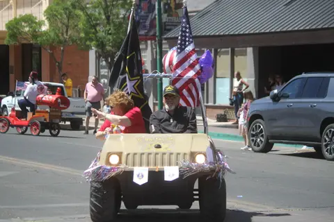 People ride in a decorated cart with flags during a parade on a city street.