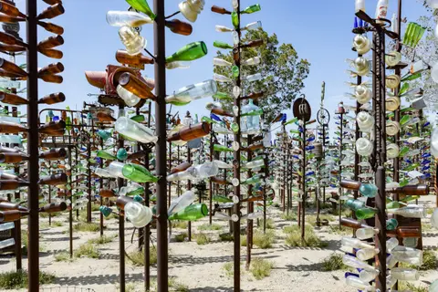 An outdoor art installation features numerous tall metal structures decorated with glass bottles.