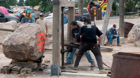 Men using a vintage drilling machine on a large rock outdoors.