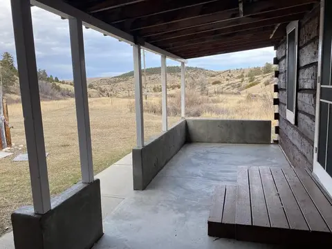 A view looking out from the covered porch of a rustic cabin toward a grassy field and hills.