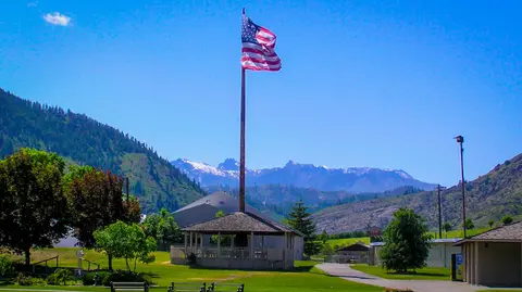 An American flag flies above a gazebo in a park with mountains in the background.