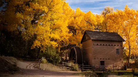 An old brick mill with a large water wheel surrounded by trees with bright yellow autumn foliage.