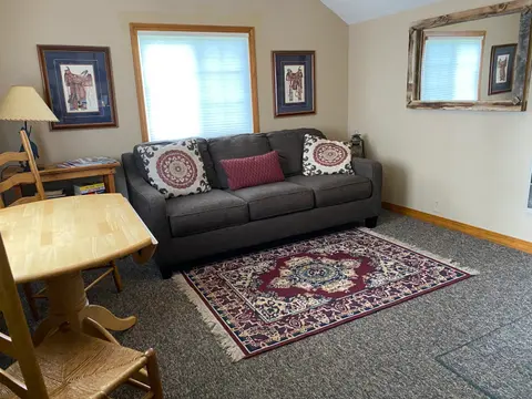 A cozy living room featuring a gray sofa, a patterned area rug, and framed artwork on the walls.