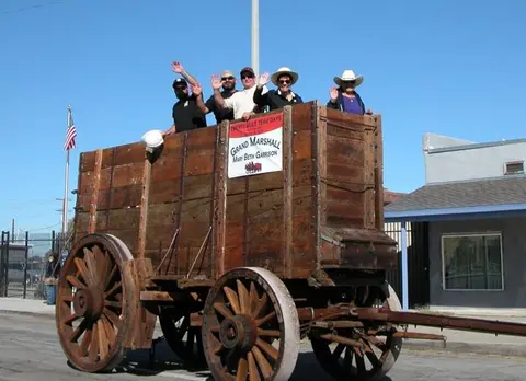 People wave from a large wooden wagon during a parade.