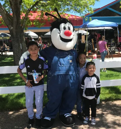 Three young boys pose for a photo with a costumed mascot character outdoors.