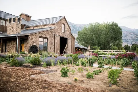 A stone and wood building stands behind a garden with mountains in the background.