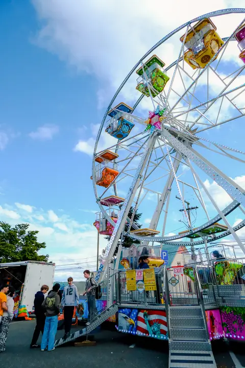 A colorful ferris wheel stands at an outdoor fair with people walking nearby.