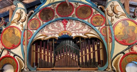 A decorative facade of a band organ featuring painted roundels and wooden pipes.