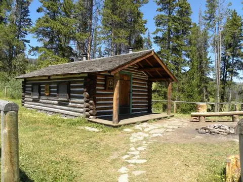 A log cabin surrounded by trees with a stone pathway leading to the porch.
