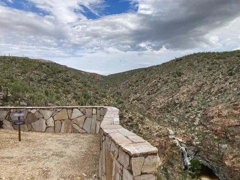 A scenic overlook with a stone wall looks out over a canyon with a waterfall.