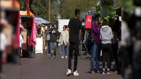 People walk along an outdoor market aisle between vendor booths.