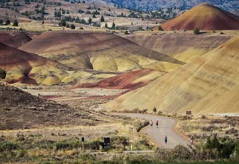 People running on a road through a landscape of colorful hills.