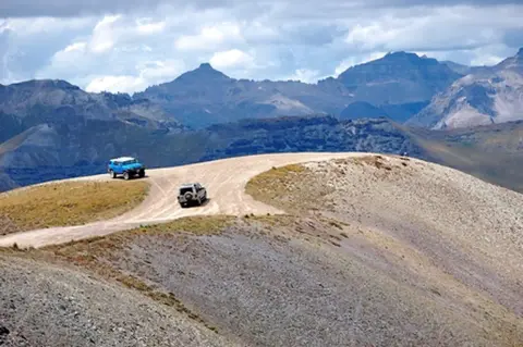 Two vehicles drive along a dirt road on a mountain ridge.