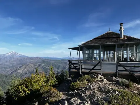 A fire lookout cabin sits on a rocky mountain peak overlooking a vast landscape.