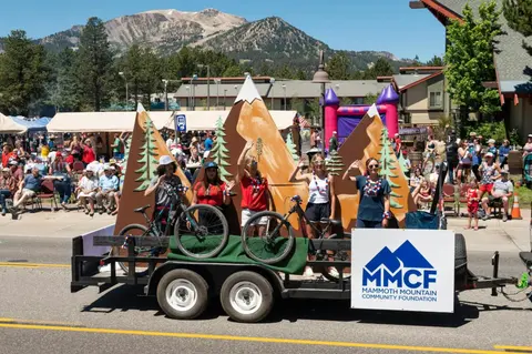 People wave from a decorated parade float with mountain props.