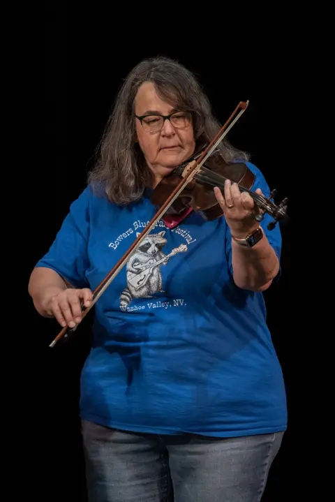 A woman plays a violin against a black background.