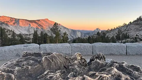 A scenic view of mountains at sunrise behind a stone wall and a textured metal relief map in the foreground.