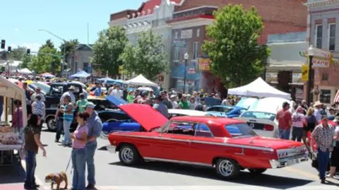 A crowded street lined with classic cars and people attending an outdoor event.