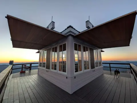 A fire lookout tower stands atop a mountain at sunset.
