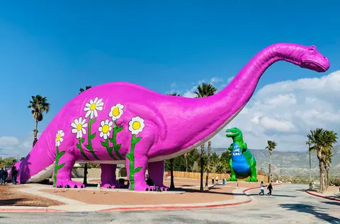 A large pink dinosaur statue decorated with white flowers stands outdoors.