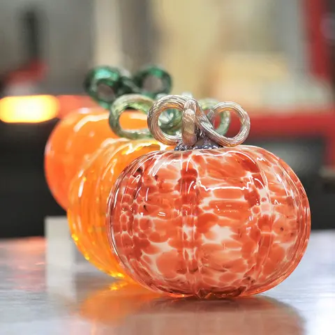 Three colorful blown glass pumpkins sit on a surface.