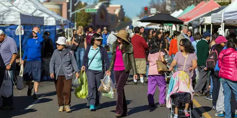 People walk along a crowded outdoor street market lined with vendor tents.