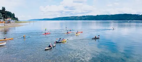 People kayaking and paddleboarding on a calm body of water near a shore.