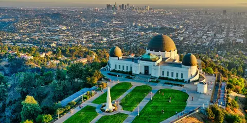 An aerial view of a large observatory building with domes overlooking a sprawling city skyline.