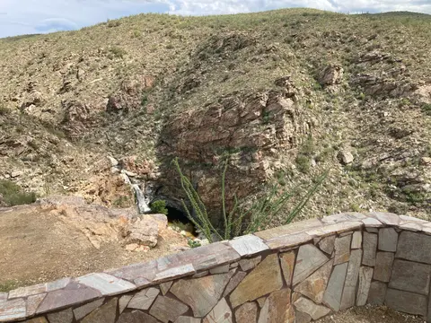 A rocky desert landscape featuring a small waterfall and a stone retaining wall.