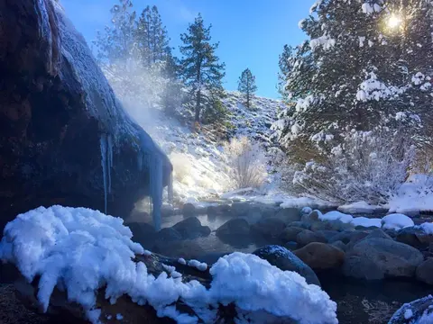 A steaming hot spring surrounded by snow and trees in winter.
