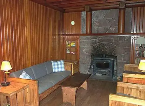 A rustic interior with wooden paneling, a sofa, and a stone fireplace.