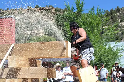 A woman uses a chainsaw to cut a large wooden log outdoors.
