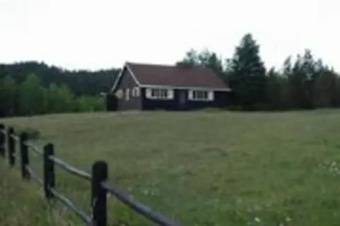 A house sits in a grassy field with a fence in the foreground.