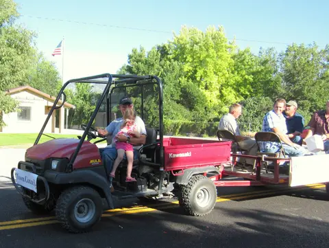 People riding in a utility vehicle and attached trailer on a paved road.