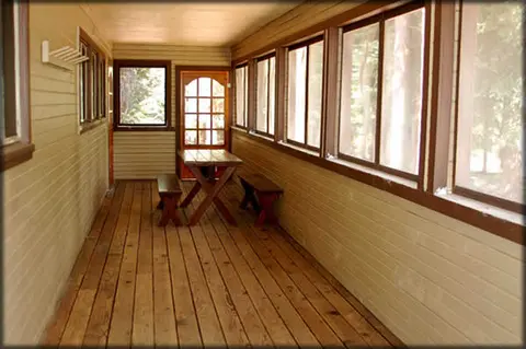 An enclosed wooden porch with large screened windows and a picnic table.