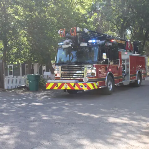 A fire engine drives down a street lined with trees and houses.