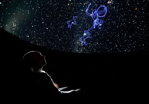 A person watches a planetarium show showing star constellations on a dome.