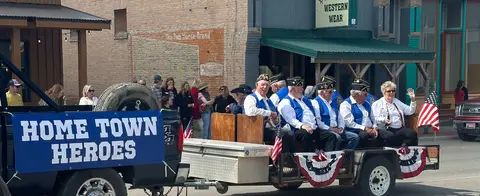A group of veterans riding in a parade on a trailer pulled by a truck.