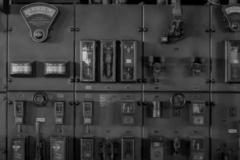 A black and white photograph of an industrial electrical switchboard with various gauges and switches.