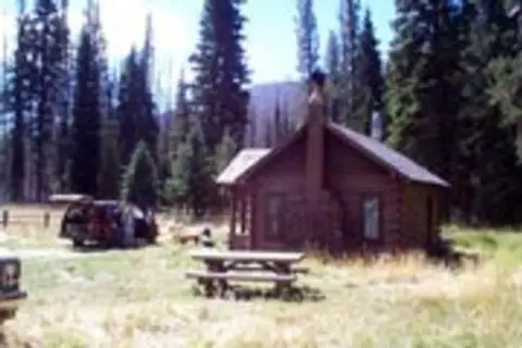 A rustic wooden cabin nestled in a forest with a picnic table in the foreground.