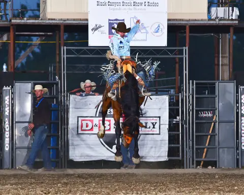 A cowboy rides a bucking horse at a rodeo arena.