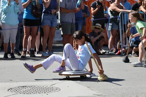 A young girl rides a wheeled object on a paved surface during an outdoor event.