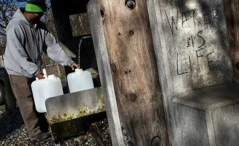 A person fills large plastic jugs with water from an outdoor spigot.