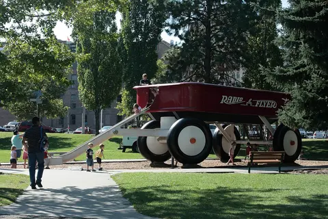 A large Radio Flyer wagon structure in a park with children playing.