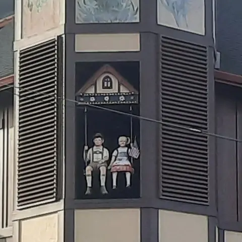 A decorative painting of two figures on a swing on the exterior of a building.