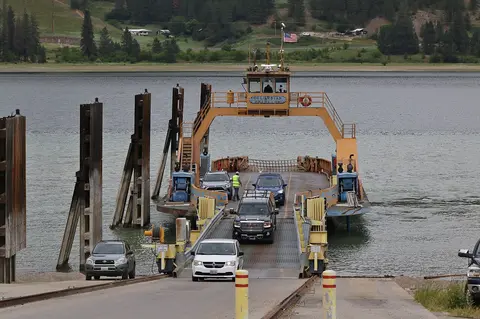 A yellow ferry transporting cars approaches a boat ramp on the water.