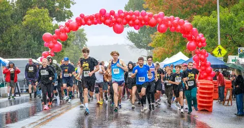 Runners participate in a race under a red balloon arch in the rain.